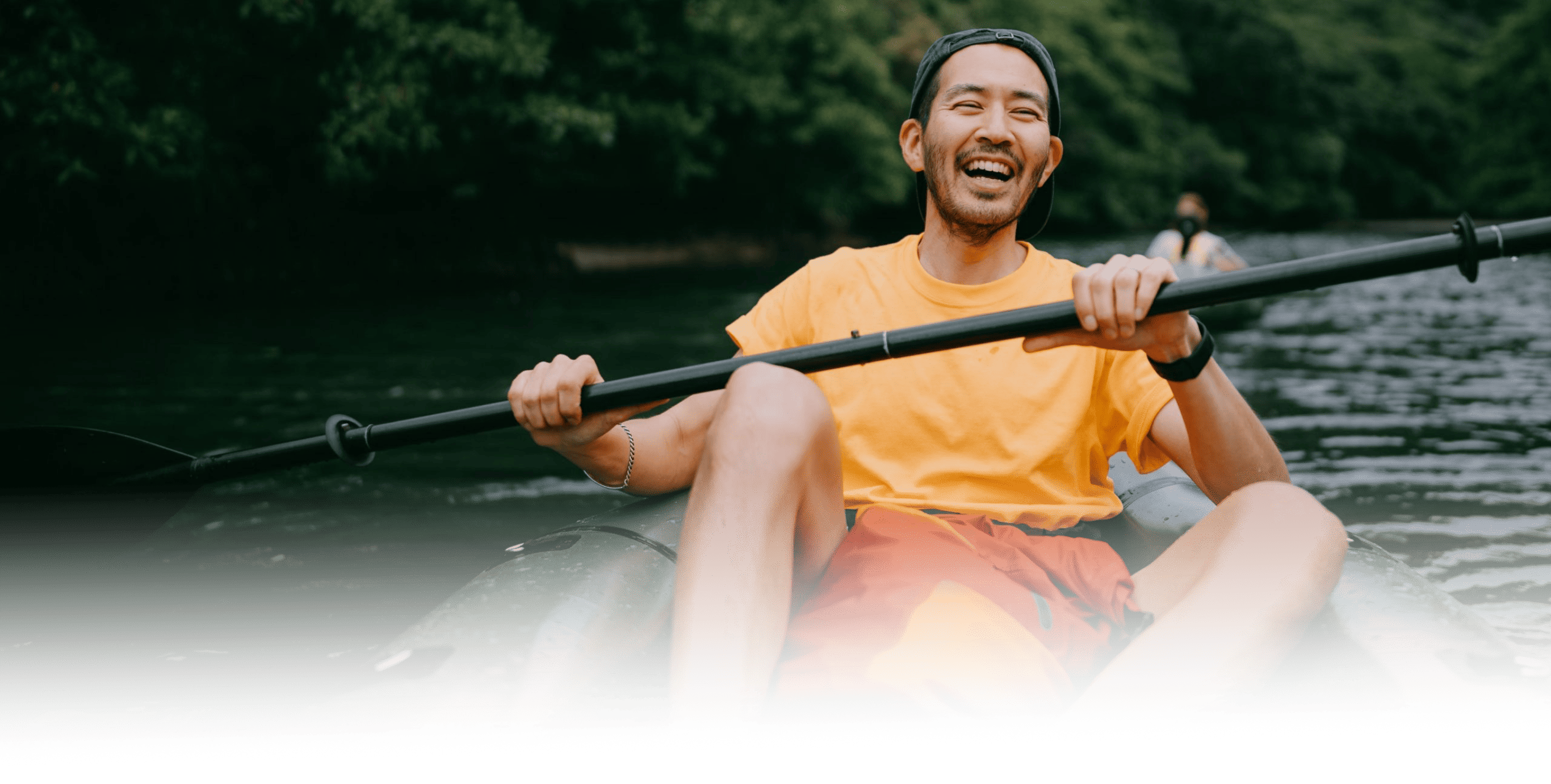 Man in a yellow shirt smiling while kayaking on a river holding a double-bladed paddle.