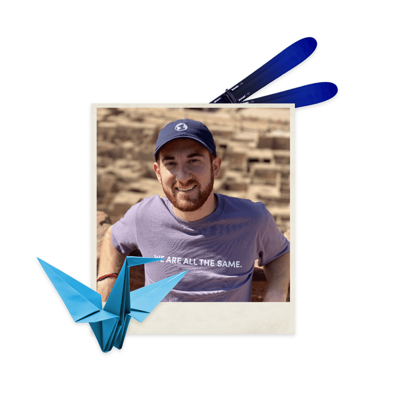 A man smiling in a baseball hat with a blue origami crane in one corner and a pair of winter skis.