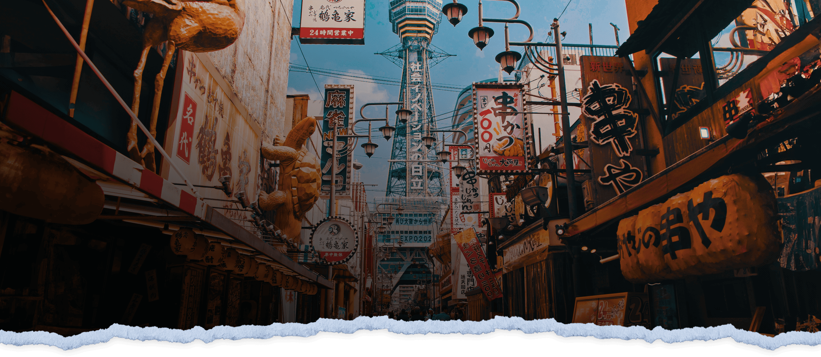 A vibrant street scene in Osaka, Japan, with various traditional signs and lanterns, including a striking blue tower visible in the background, set under a clear sky.